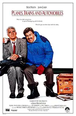 Sitting on a bench, John Candy's Del Griffith, dressed in a winter outfit, puts his arm around Steve Martin's Neal Page, dressed in a suit, while holding a coffee cup; the latter appears discomforted. Griffith's large luggage is on the floor next to him, while Page's suitcase sits on his lap.