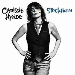 A black-and-white photo of Hynde in arm's akimbo pose featuring a white background behind her; her face is painted in the order blue, yellow, and black. The album name "Stockholm" is in the left side of background in black letters, and on the right is her name in blue.