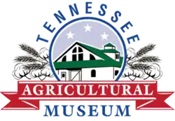 Green barn building surrounded by wheat and the name of the museum