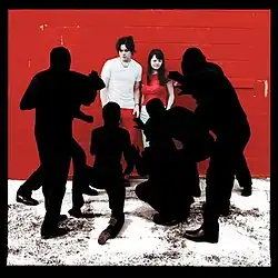 A male and female stand are pestered by black silhouettes in front of a brick wall on what appears to be snowy ground. A black border outlines the artwork. Dominant colors are red, black, and white.